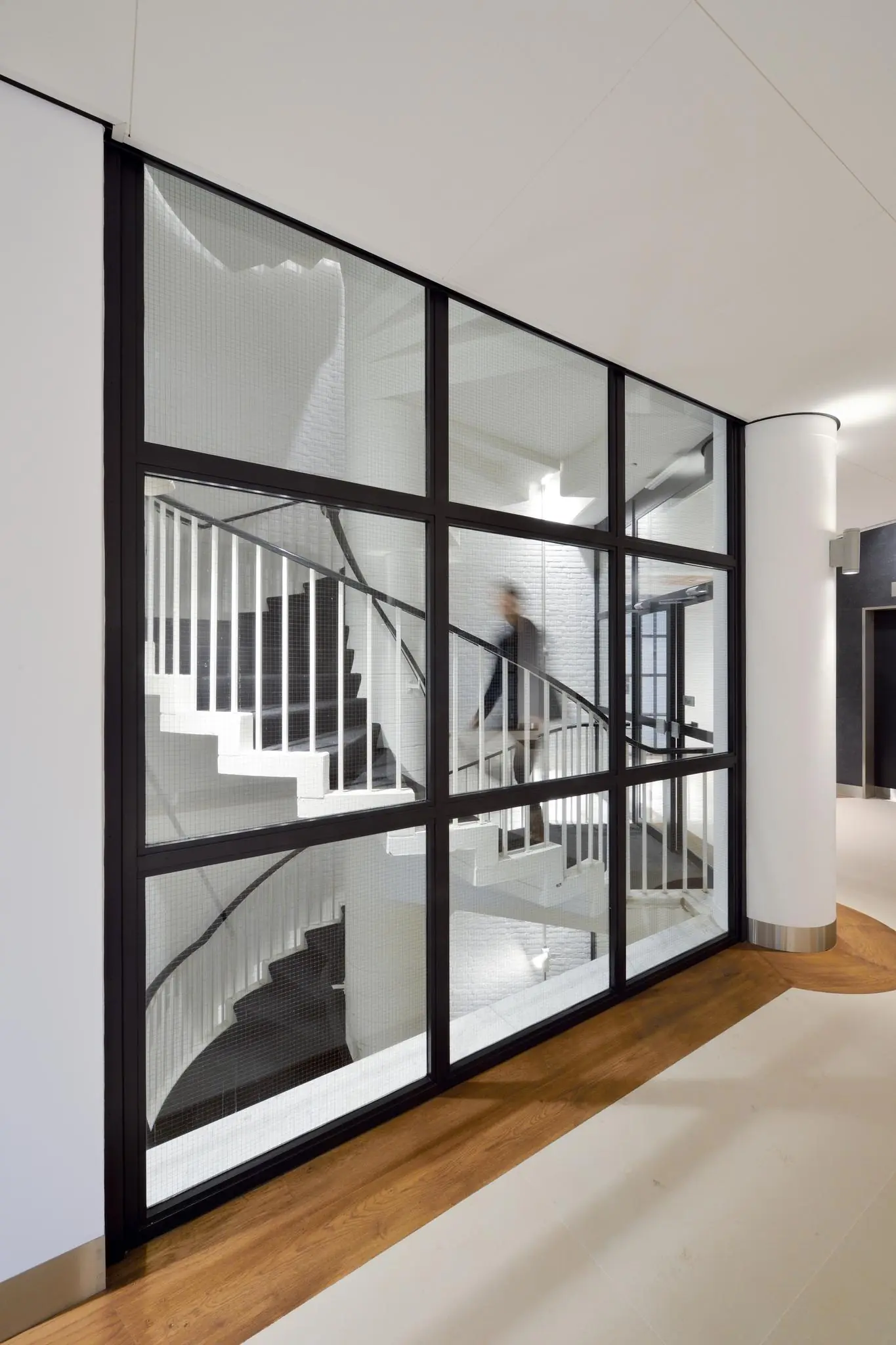 Doorkijk op een modern trappenhuis met witte wenteltrap achter een glazen wand in het gebouw aan de Floris Grijpstraat.